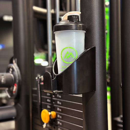 A white Maximus Athletics shaker bottle with a green logo, attached to a black fitness machine.