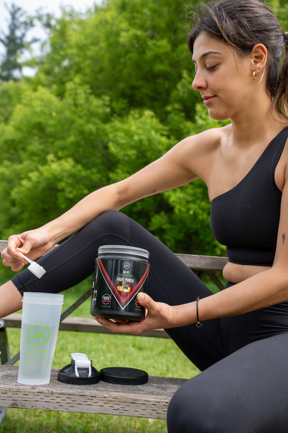 Woman sitting outdoors holding a supplement container and a tumbler.